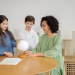 A teacher and two children explore a globe together in a classroom setting.