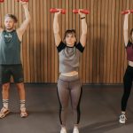 Three adults exercising with dumbbells in a gym setting, promoting fitness and healthy lifestyle.