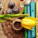 Top view stack of books on table near beautiful yellow tulip and orchid flowers arranged with chocolate truffles placed on wicker placemat